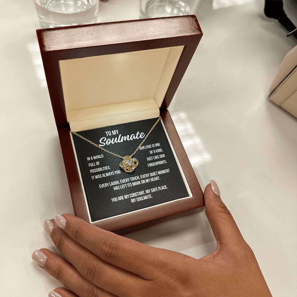 Hand holding open gift box with yellow gold Love Knot Necklace and black soulmate message card