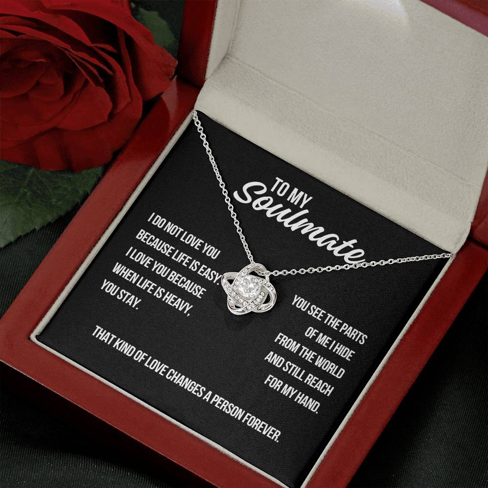 Angled view of white gold love knot necklace on black soulmate message card beside a red rose